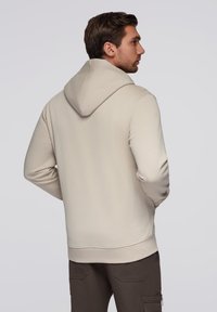 Felpa con cappuccio beige in tessuto strutturato, dotata di tasca a marsupio e polsini a coste. Indossata con pantaloni cargo scuri.