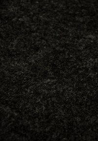 Tela de lana oscura con una superficie suave y texturizada, con fibras claras y oscuras entrelazadas, creando una profundidad sutil en el material.