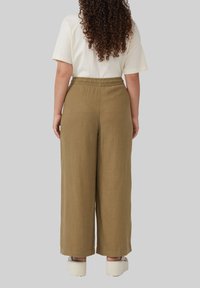 Pantalons en lin kaki, à taille haute et coupe ample, avec une texture lisse, une ceinture élastique et des jambes larges, associés à des chaussures blanches décontractées.