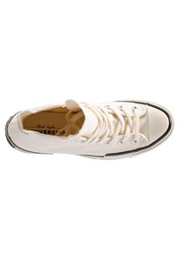 Biele plátené tenisky s okrúhlym špičkou, čiernou gumovou podrážkou a striebornými očkami. Obsahujú klasický dizajn na šnurovanie a branding Chuck Taylor vo vnútri.