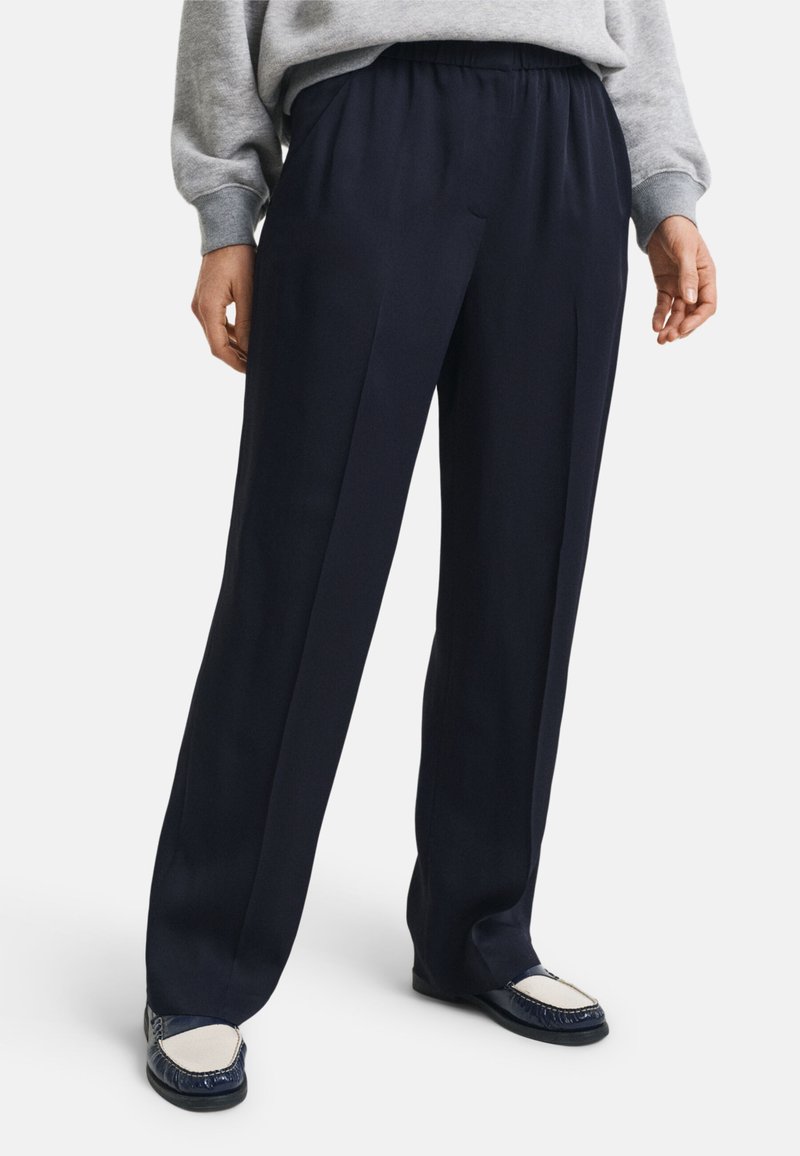 Pantaloni navy con una vestibilità rilassata, realizzati in tessuto morbido, con un cintura elastica, due pieghe anteriori e una texture liscia.
