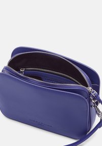 Borsa a tracolla viola in pelle con una texture liscia, scomparti con doppia zip, hardware silver e una tracolla removibile.