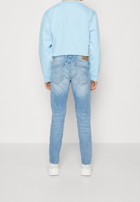 Ljusblå sweatshirt och ljusa tvättade denimjeans med en slät yta. Jeans har en bakficka och rundad sömnad på fickorna. Vita sneakers.