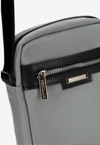 Borsa a tracolla in tessuto grigio con dettagli in pelle nera e hardware in argento; dotata di una tasca con zip e logo del marchio impresso.