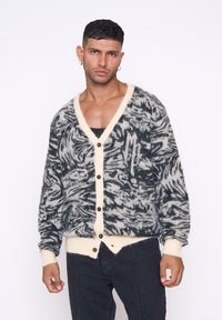 Strickjacke mit einem schwarzen und cremefarbenen abstrakten Muster, V-Ausschnitt und braunen Knöpfen, mit gerippten Manschetten und Saum.