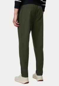 Pantaloni verde oliva, texturizzati, con una vestibilità comoda, dotati di vita elastica e tasca sul retro, indossati con scarpe da ginnastica bianche.