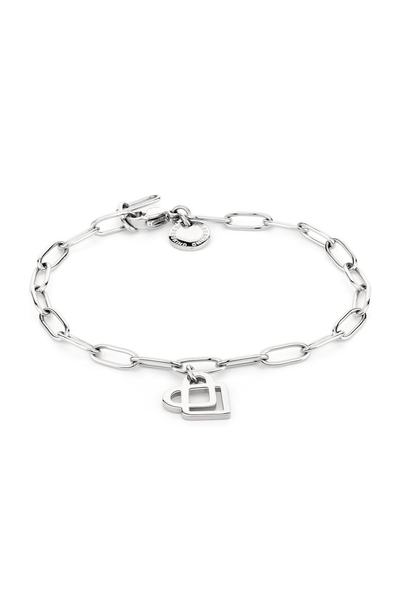 Pulsera de cadena de metal plateado con eslabones alargados, que presenta un charm en forma de corazón y una pequeña etiqueta circular con texto grabado.