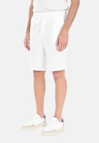Pantaloni corti bianchi in lino con vita elastica e cordino. Presentano tasche laterali e una vestibilità comoda, indossati con sneakers bianche.
