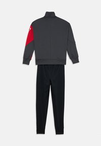 Completo sportivo con giacca zip grigia scura con accento rosso sulla spalla sinistra e pantaloni neri affusolati, realizzati in un tessuto morbido.