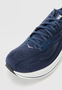 Scarpa running navy con upper in rete testurizzata, dettagli rinforzati e un'intersuola bianca. Presenta lacci piatti e perforazioni per la traspirabilità.