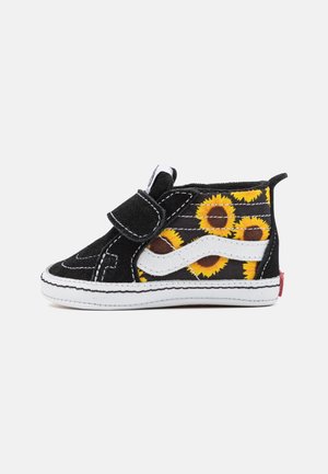 Scarpa alta in tessuto nera con stampa di girasoli gialli, fascia in Velcro, accenti bianchi e suola bianca con cuciture dettagliate.