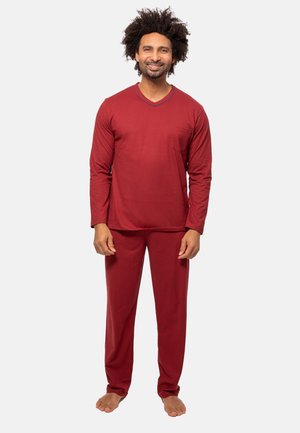 Man standing barefoot wearing matching red long-sleeve top and pants, smiling against a plain light background.