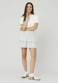 Jupe courte blanche avec volants superposés et petits motifs floraux bleus, assortie à un t-shirt blanc et des baskets blanches avec des accents noirs.