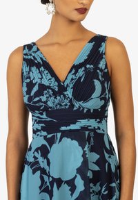 Abito plissettato blu navy con motivo floreale turchese, scollatura a V profonda e vita aderente. Presenta un tessuto liscio e leggero in un design elegante.