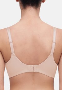 Beige bh med justerbare stropper, glat stof og en hægte- og øjeslukning bagpå. Har et sømløst design og minimalistisk stil.