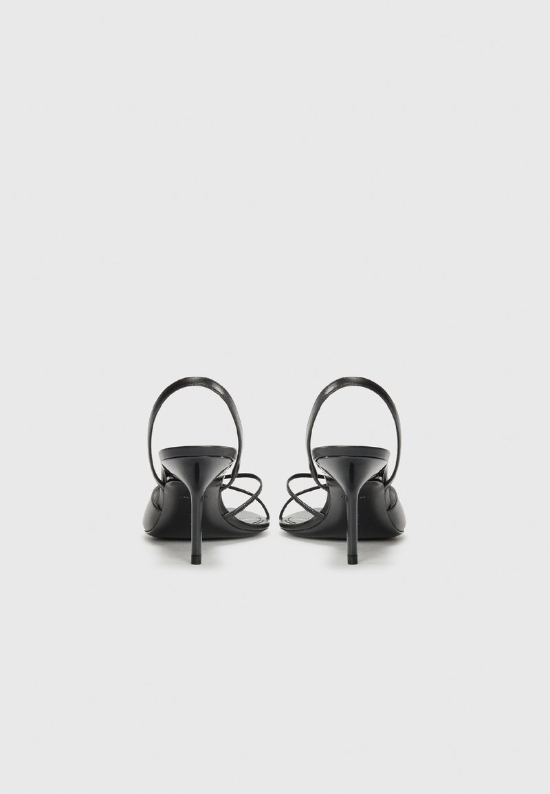 Sandales à talons hauts noires avec une finition en cuir lisse, dotées de fines brides de cheville et d'un talon élancé, mettant en avant un design minimaliste.
