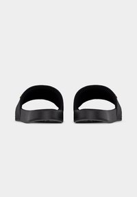 Schwarze Slip-On-Sandalen mit breiten Riemen und strukturierten Fußbetten, von hinten auf einem schlichten weißen Hintergrund gezeigt.