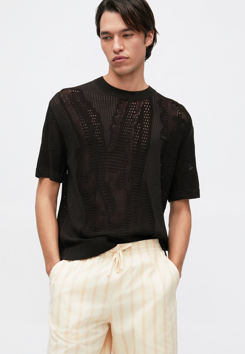 Pull en tricot noir à manches courtes avec un motif texturé et un col côtelé, associé à un short léger à taille élastique à rayures.