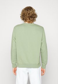 Sudadera verde claro con cuello redondo acanalado y mangas largas, que presenta un dobladillo recto y una textura de algodón suave.