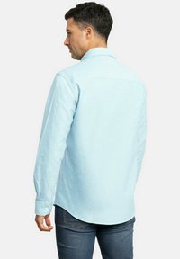 Camisa de manga larga azul clara con un cuello estructurado, una textura sutil y puños abotonados. La vista trasera muestra un dobladillo curvado y un ajuste entallado.