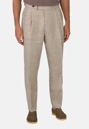 Beige linnen broeken met een gestructureerde afwerking, voorzien van voorplooien en een tailleband met een enkele knop. Gecombineerd met bruine schoenen.