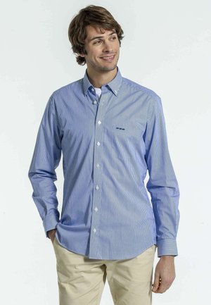 Chemise à manches longues à rayures bleues et blanches, fabriquée en tissu léger, dotée d'un col boutonné et d'un petit logo sur la poitrine.