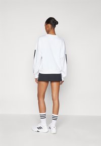 Hvit genser med svarte ermer, kombinert med et svart skjørt. Modellen har på seg hvite joggesko og stripete sokker. Glatt, uformelt design.