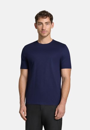 Camiseta de manga corta de color azul marino, hecha de una tela suave, con un escote redondo y un corte relajado, llevada con pantalones oscuros.