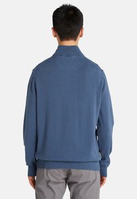 Maglione blu lavorato a maglia con colletto alto e polsini a costine. Tessuto morbido con taglio dritto e senza motivi o accessori visibili.