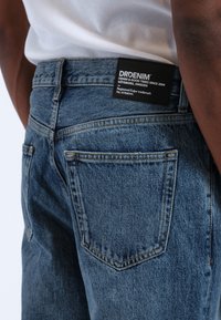 Tummansininen farkkutakki, jossa on takapaneelissa "DRDENIM"-logo. Kankaassa on teksturoitu pinta, klassiset taskusaumat ja tyylikäs istuvuus.