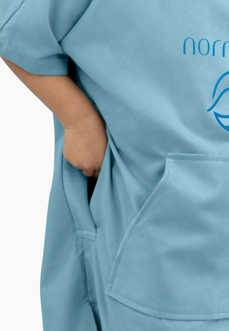 Blaues Kleidungsstück mit kurzen Ärmeln, das eine Tasche an der Seite aufweist. Das Material wirkt weich und strukturiert, mit einem aufgedruckten Logo auf dem Stoff.