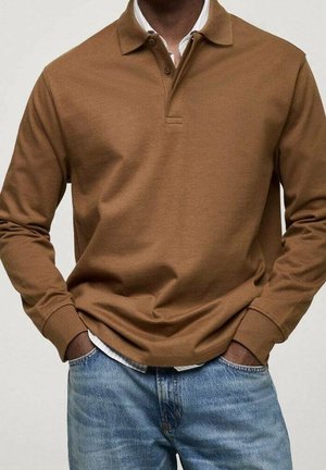 Polo marrón de manga larga hecho de algodón, con cuello de solapa y botones. Se lleva puesto sobre una camisa blanca con cuello y unos vaqueros azules.