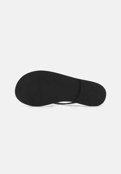 Suela de sandalia negra con una textura suave, bordes redondeados y un diseño minimalista; presenta un logotipo sutilmente embossado en la superficie.