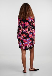 Robe fleurie à manches longues, taille cintrée, fond noir avec de grandes fleurs roses et violettes. Tissu lisse, coupe mi-genou.