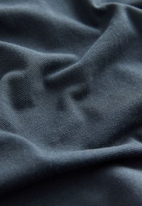 Mörkgrått tyg med strukturerad väv, tydliga veck och mjuk yta. Närbild som framhäver material och djup.