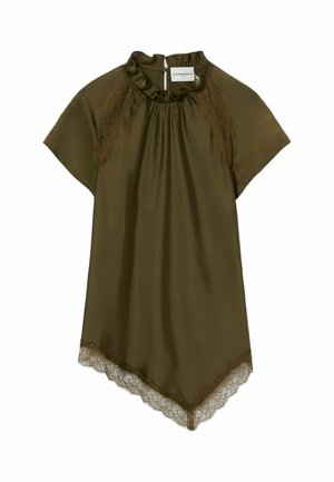 Donna con vestito verde oliva che tiene una grande borsa bordeaux, indossa scarpe sportive nere con lacci bianchi e calzini grigi, in piedi su uno sfondo bianco.