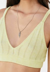 Kobieta w jasnopomarańczowym dzianinowym bralecie z pionowymi oczkami i srebrnym naszyjnikiem z abstrakcyjnym wzorem.