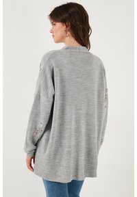 Suéter de punto gris con un corte relajado, adornado con colorido bordado floral en las mangas y un escote redondo. Textura suave.