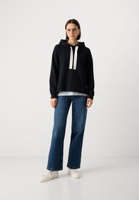 Juoda gobtuvu puloveris su baltais raišteliais, turintis atsitiktinį fasoną. Suderintas su plačiais mėlynais džinsais ir baltais sportbačiais. Minimalistinis dizainas.