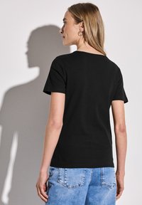 Černé žebrované tričko s krátkými rukávy, kulatým výstřihem a obepnutým střihem. Nosič zvolil světle modré džíny šortky.