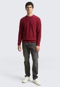 Pull en tricot rouge avec un motif texturé, col rond, poignets et ourlet côtelés. Assorti avec un jean gris et des baskets blanches.