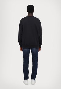 Hanorac negru cu gât rotund și mâneci lungi, asortat cu blugi slim-fit de culoare albastru închis și adidași albi. Design simplu, casual.