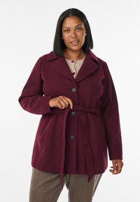 Burgundy coat with large collar and a belted waist, featuring prominent black buttons and long sleeves, made of a soft, textured fabric.