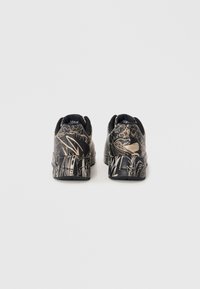 Des sneakers noires arborant un design graphique doré détaillé, une surface texturée et une semelle rembourrée pour le confort. La vue arrière montre le talon et le design.