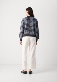 Strikket blå og sort sweater med et bladmønster, ribbede manchetter og kant. Kombineret med hvide bukser med vidde og sorte slip-on sko.