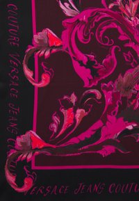 Bufanda negra con audaces patrones florales en rosa y rojo. El texto en los laterales dice "COUTURE VERSACE JEANS COUTURE." Textura suave.