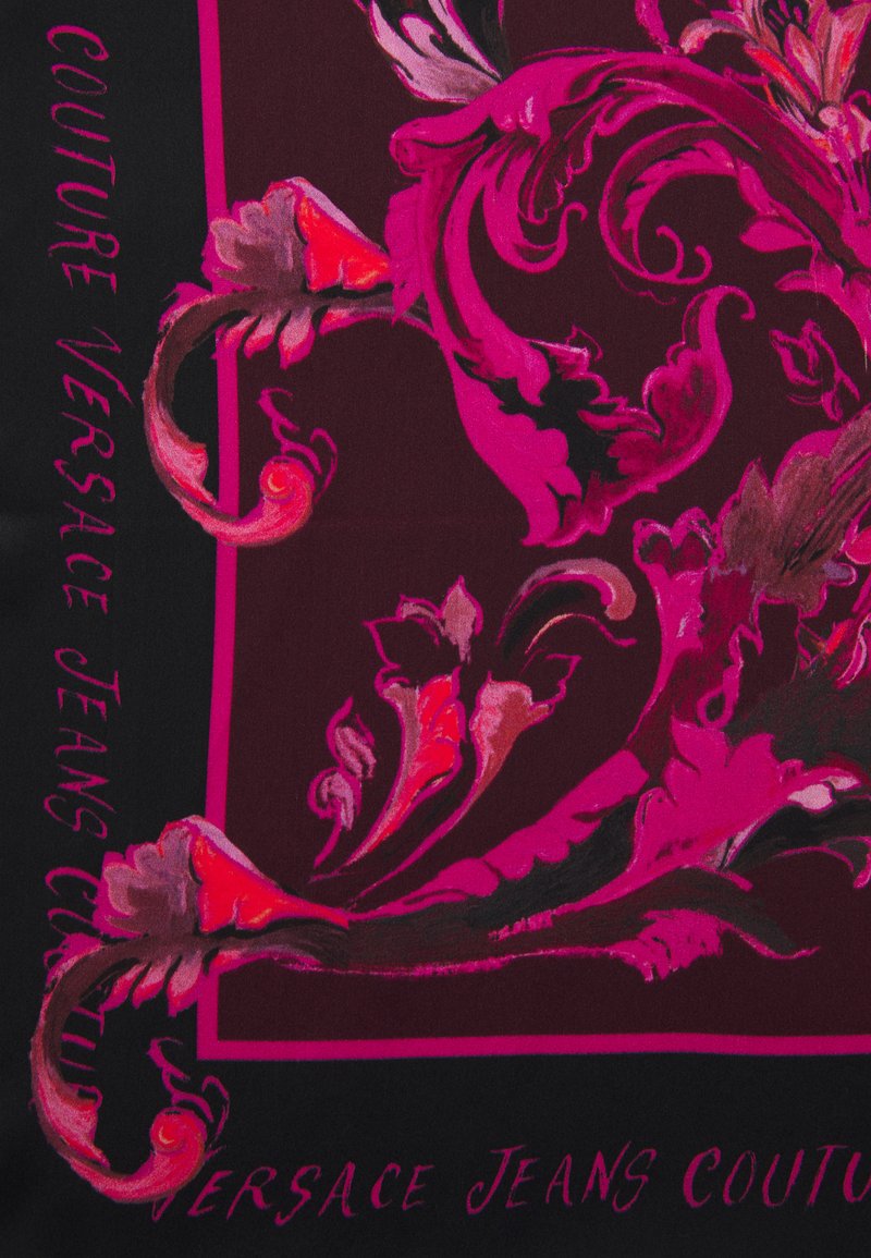 Bufanda negra con audaces patrones florales en rosa y rojo. El texto en los laterales dice "COUTURE VERSACE JEANS COUTURE." Textura suave.