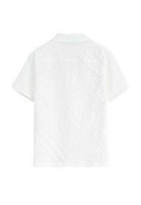 Chemise à manches courtes en tissu blanc texturé avec un motif en losange, dotée d'un col et d'un bas droit, vue du dos.
