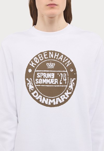 White long-sleeve shirt featuring a textured pattern and a circular brown graphic with "KØBENHAVN," "SPRING/SOMMER," and "DANMARK."