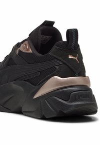 Scarpa sportiva nera con tomaia in rete e materiale sintetico, dettaglio in rosso metallizzato sul tallone, suola testurizzata e logo sul tallone e sulla linguetta.